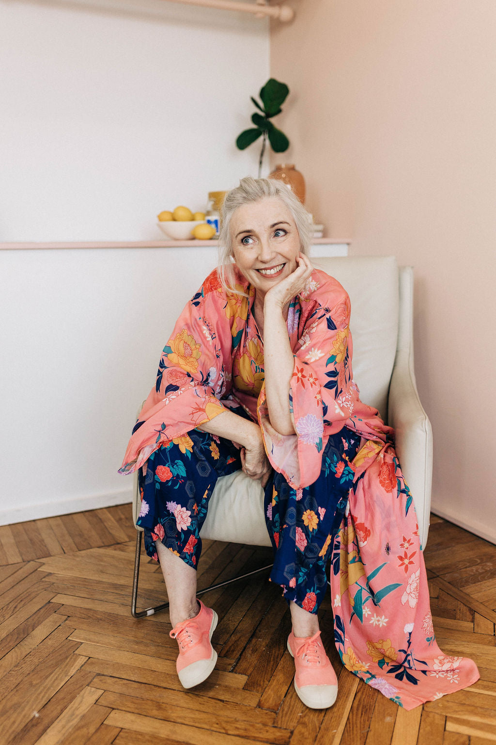 woman sitting in a chair smiling wearing bright colourful pants, top and pink floral chimono robe