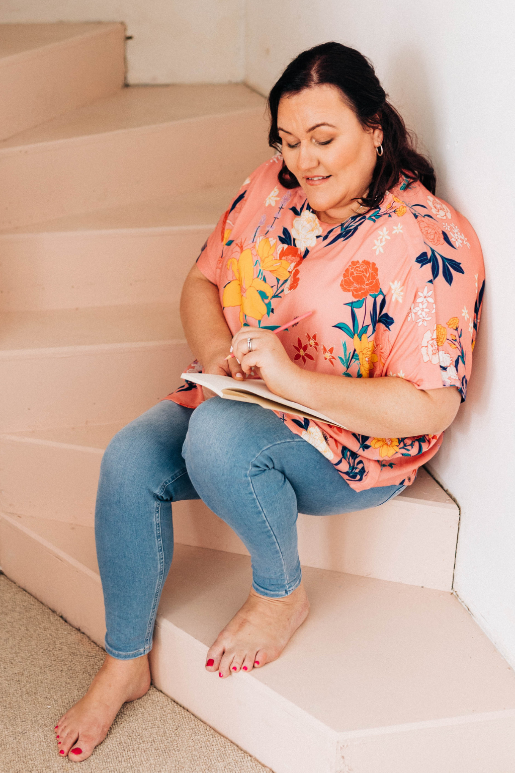 woman wearing pink floral adaptive top and jeans sitting writing in her journal